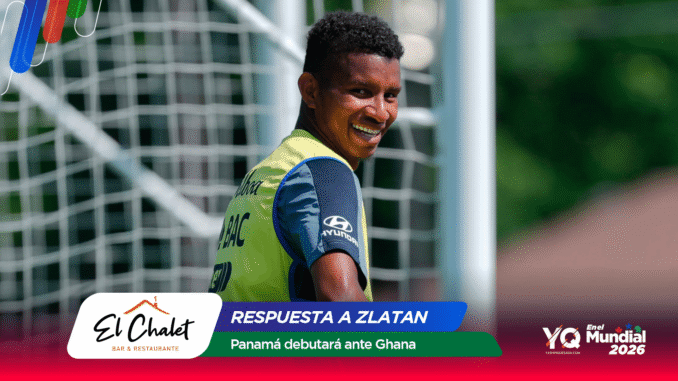Soccer player in a yellow training bib smiling at the camera near a goal net.