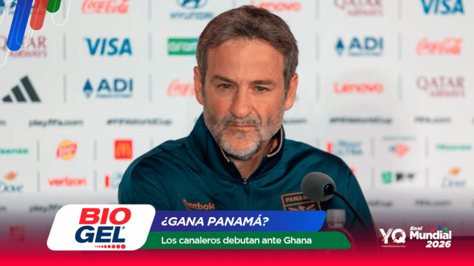 Man at a press conference speaking into a microphone, wearing a dark teal sports jacket, with sponsor logos on the backdrop and foreground banner obscuring part of the view.