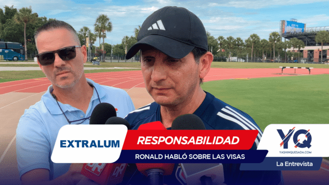 Two men speak to reporters at an outdoor track field, microphones in view and a large graphic banner reading EXTRALUM and RESPONSABILIDAD covering the lower foreground.
