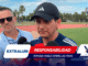Two men speak to reporters at an outdoor track field, microphones in view and a large graphic banner reading EXTRALUM and RESPONSABILIDAD covering the lower foreground.