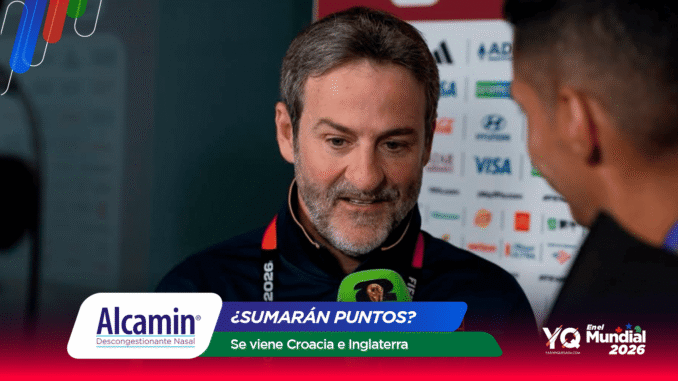 Man with gray beard being interviewed at a press area, with sponsor banners and a green microphone in the foreground.