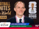 Portrait of a smiling man in a dark suit and pink lanyard at a FIFA World Cup 2026 event, with banners in the background reading 'Football Unites the World' and 'FIFA World Cup 2026'.