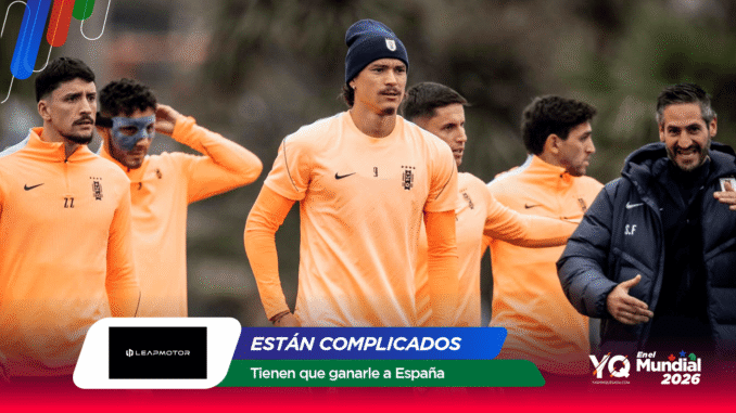 Equipo de fútbol entrenando al aire libre con camisetas naranja; varios jugadores de pie y un entrenador a la derecha con chaqueta oscura.