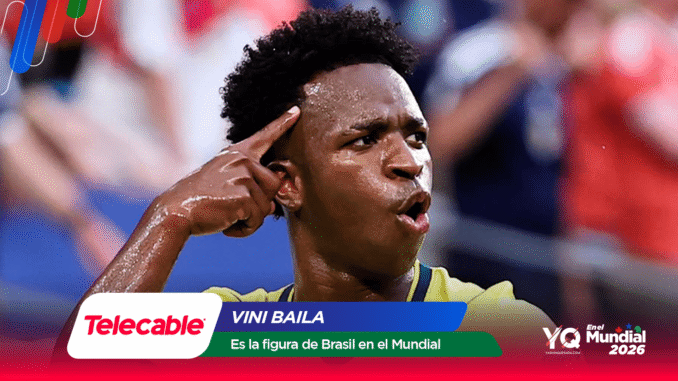 Brazilian footballer celebrates a goal, pointing to his temple with a sweaty yellow jersey and a blurred stadium crowd behind; sponsor graphics at the bottom.