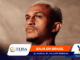 Close-up portrait of a man looking upward with a promotional banner at the bottom showing 'BAJA EN BRASIL' and sponsor logos.