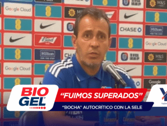 Man in a blue polo speaking into a microphone at a press conference, with a sponsor-wall backdrop full of logos (Chase, Nike, Google Cloud, M&S, Hilton) and a red-white banner in the foreground.
