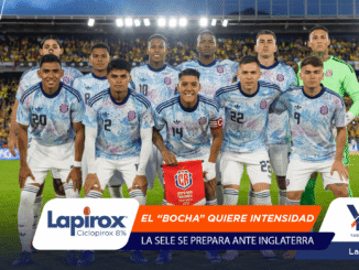 Group of Costa Rica soccer players pose for a team photo on the field, with a crowded stadium and bright banners in the foreground.
