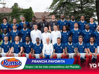 France football team group portrait outdoors: players in blue kits with white collars pose in rows with coaches, against a grassy field and trees; colorful banners at bottom of image.