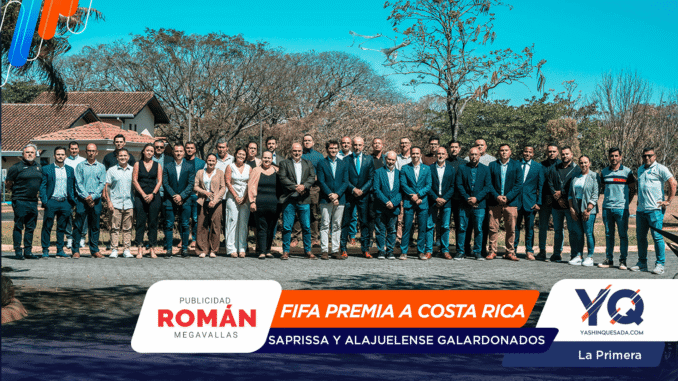 Large group of professionals in suits and smart casuals posing outdoors for a group photo, with sponsor banners along the bottom edge.
