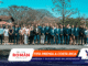 Large group of professionals in suits and smart casuals posing outdoors for a group photo, with sponsor banners along the bottom edge.