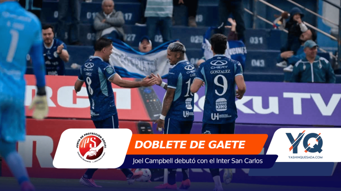 Blue-clad soccer players celebrate with a high-five on the pitch, banners and crowd in the background