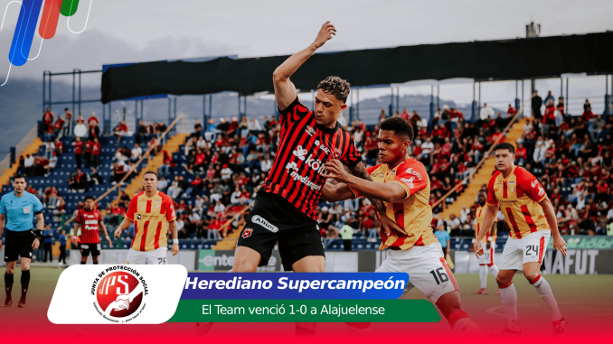 Soccer players duel for the ball on a crowded stadium pitch, with a banner announcing Herediano Supercampeón and the 1-0 victory text overlay.
