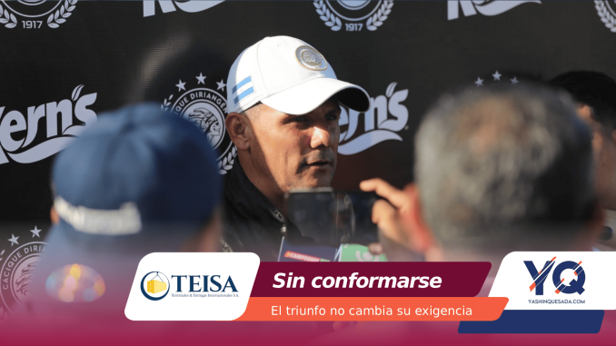Man wearing a white cap speaks to reporters at a press conference with sponsor logos in the background.