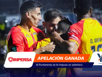 Soccer players in red and yellow celebrate in a huddle on the field at night, arms around teammates.
