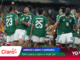 Mexican national team players in green jerseys celebrate on the field, numbers 23 and 25 visible, stadium crowd in background.