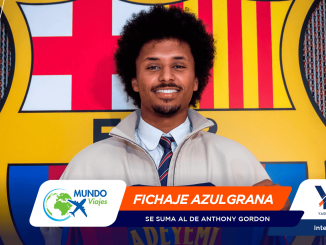 Portrait of a smiling man in a light jacket and striped tie, standing in front of a bold, colorful mural with a lower banner reading 'FICHAJE AZULGRANA' and logos visible at the bottom edge.