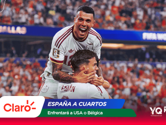 England footballers celebrate a goal, lifting a teammate amid a packed stadium and sponsor banners nearby.