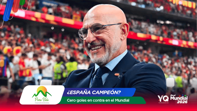 Smiling bald man in a suit at a stadium with colorful banners and a cheering crowd in the background (celebration scene).