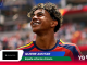 Smiling young soccer player in a red‑blue jersey looks upward, stadium crowd blurred in the background (promo banner image).