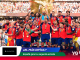 Spanish men's football team celebrating on a podium with the trophy and medals after their victory, surrounded by confetti in a packed stadium.