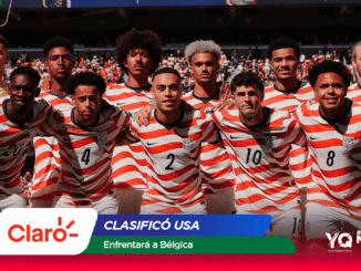 United States men's soccer team posing together on the field in red and white striped jerseys with a crowd in the background.