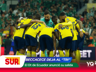 Football team in yellow uniforms huddle on the pitch around a teal-clad goalkeeper with a green stadium crowd behind them.