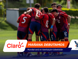 Group of soccer players in red uniforms huddling on a green field.