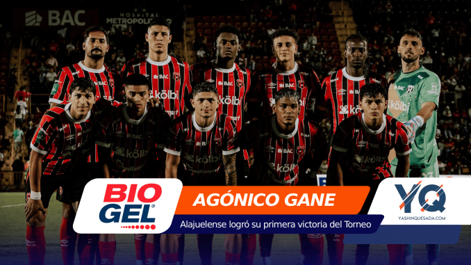 Group of soccer players in red-and-black striped uniforms pose for a team photo on the field at night, with a goalkeeper in a green kit on the right and a bold sponsor banner across the foreground.