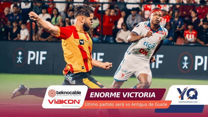 Two soccer players sprint to the ball during a match, one in a yellow-red jersey and the other in white with blue accents, with a cheering crowd in the stands behind them.