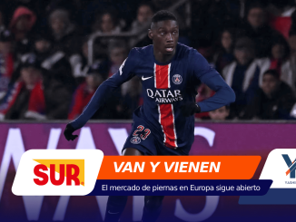 Soccer player in PSG kit runs on the field during a match, 광고 banners in the foreground and crowd in the stands behind him.
