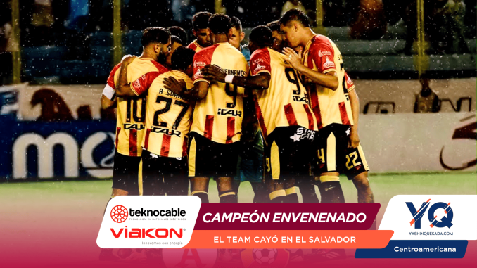 Soccer players in yellow and red striped jerseys huddle in celebration on a rain-soaked field, with sponsor banners visible at the bottom.