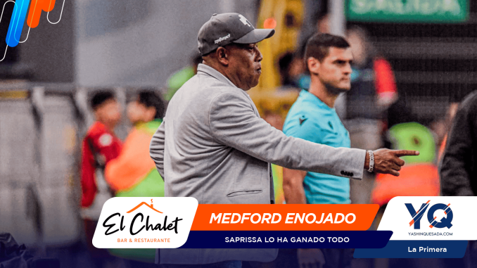 Coach in a gray blazer points to the right on the sideline, with event banners and logos across the bottom of the scene.