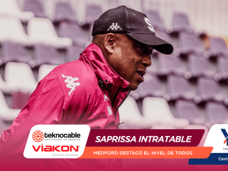 Profile of a man in a pink jacket and cap at a bleacher-filled stadium, with sponsor banners across the bottom indicating a promotional event.