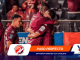 Soccer players in maroon uniforms celebrate on the field, embracing and smiling after a goal.