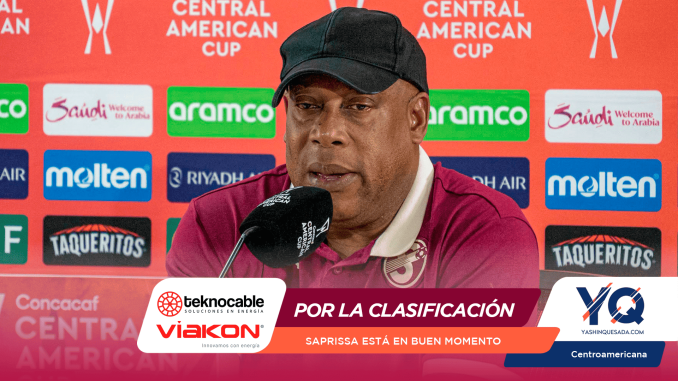 Man in a maroon polo and black cap speaks into a microphone at a press conference backdrop featuring Central American Cup logos and sponsors.